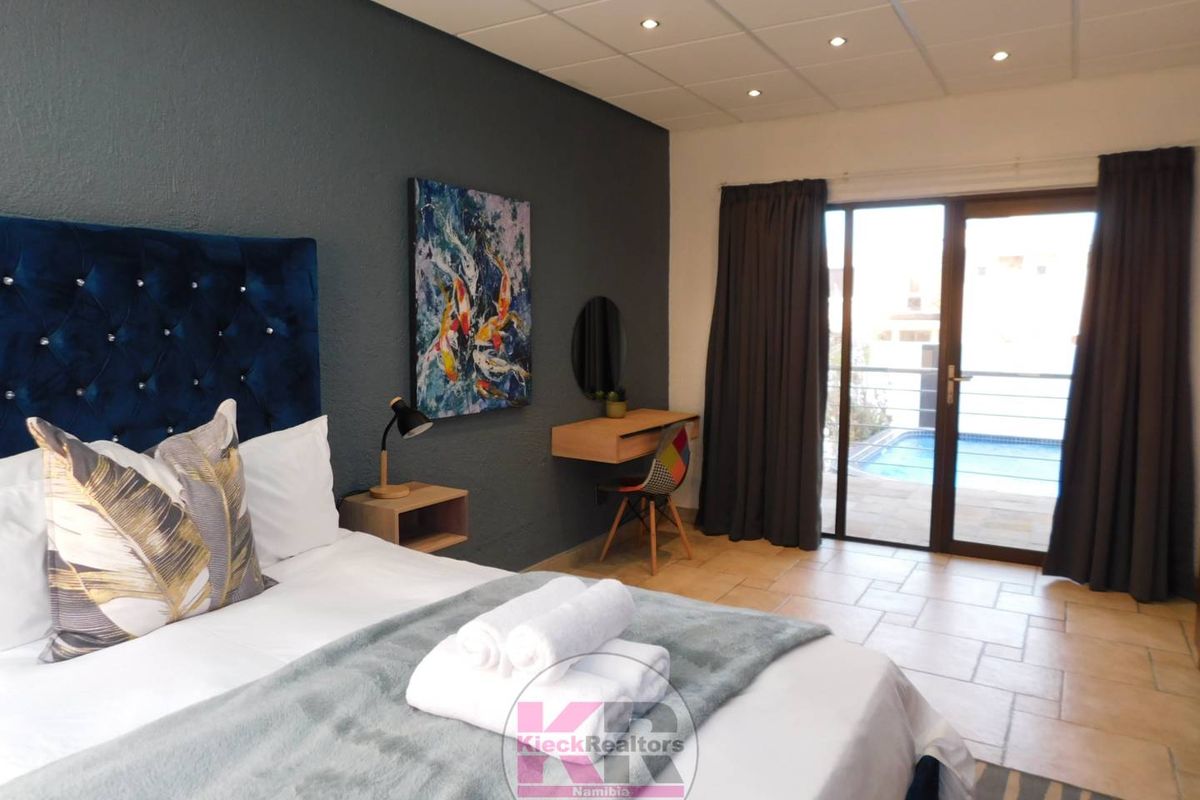 Spacious bedroom featuring tiled flooring, recessed ceiling lighting, and a sliding glass door providing direct access to the outdoor pool area.