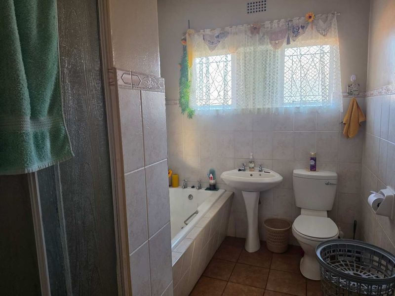 A functional bathroom featuring a pedestal basin, built-in bathtub, and a separate shower enclosure with tiled finishes throughout.