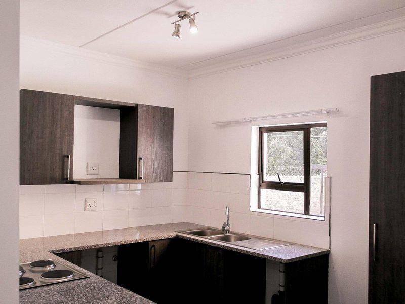 A clean, functional kitchen featuring dark wood cabinetry, granite countertops, a double bowl sink, and an integrated electric hob with tiled splashbacks.