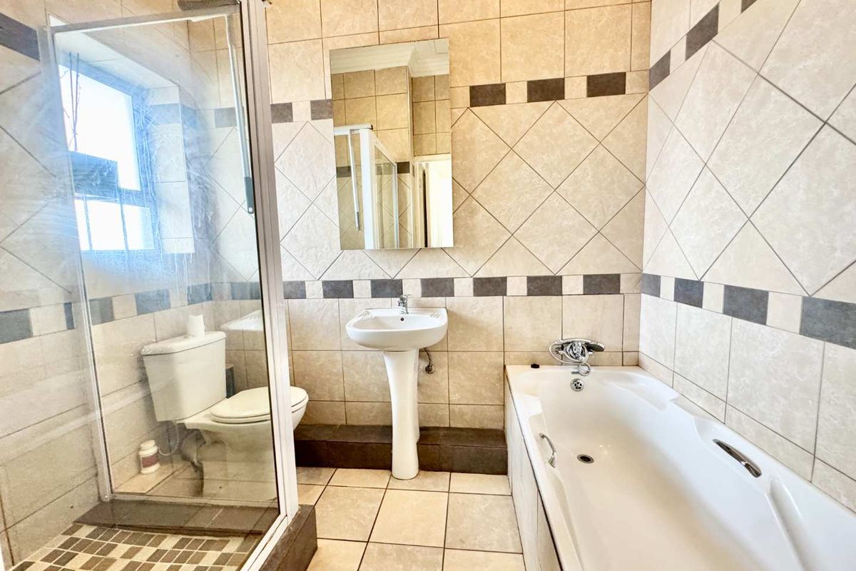A functional bathroom featuring a separate shower enclosure, a bathtub, a pedestal basin, and tiled walls and flooring.