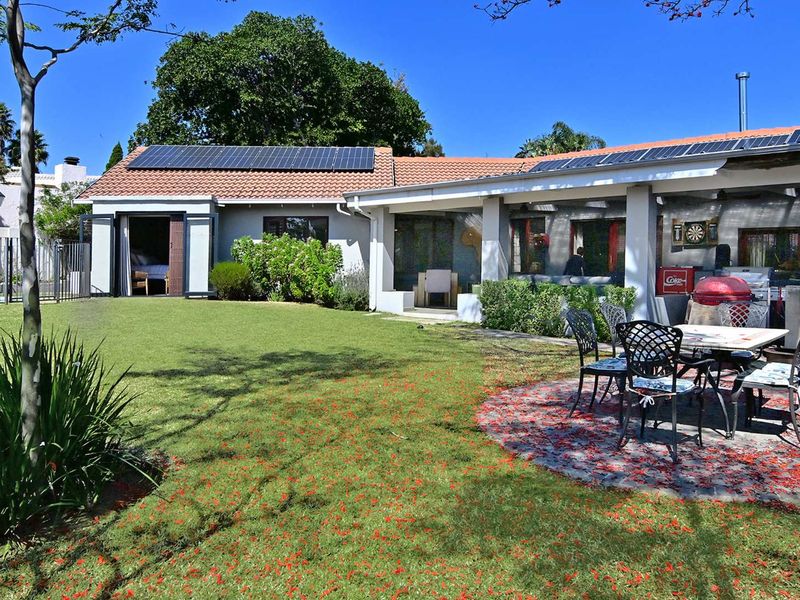 Rear view of the property featuring a landscaped garden, a paved patio area, and a roof equipped with solar panels.