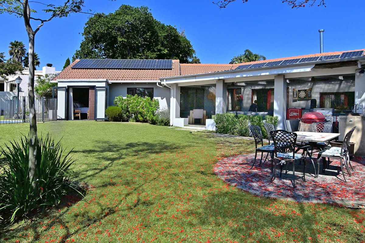 Rear view of the property featuring a landscaped garden, a paved patio area, and a roof equipped with solar panels.