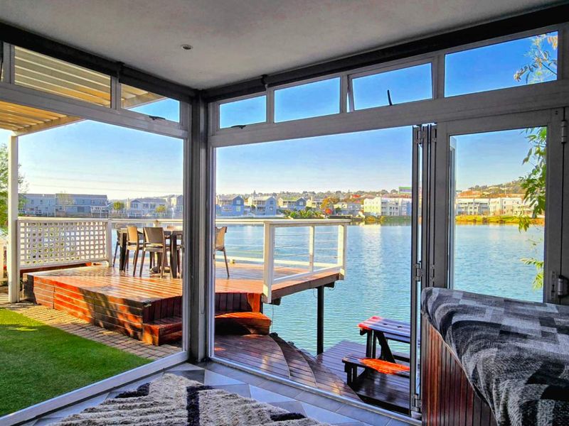 A bright, enclosed patio area featuring expansive bi-fold glass doors that open onto a timber deck overlooking the water.