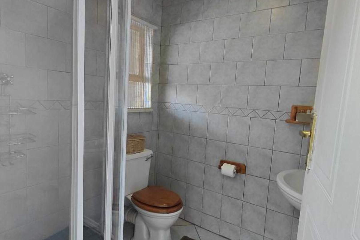 A functional bathroom featuring a curved glass shower enclosure, pedestal basin, and flush toilet with neutral ceramic wall and floor tiling.