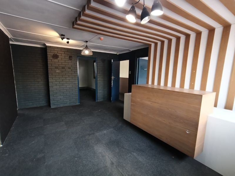 Modern industrial-style reception area featuring a built-in timber desk, decorative slat ceiling detail, and an exposed brick feature wall.