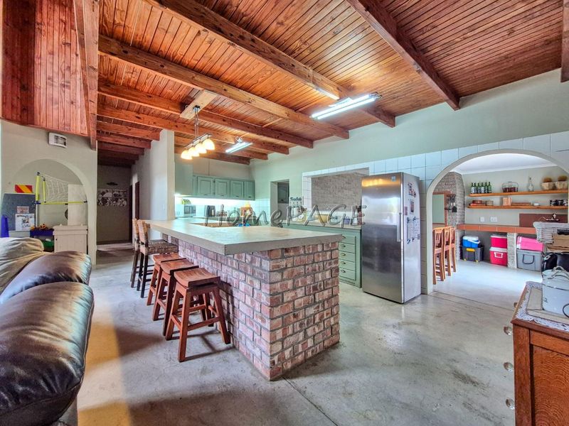Spacious open-plan kitchen and living area featuring exposed timber beam ceilings, a rustic brick island with concrete countertop, and tiled archway transitions.