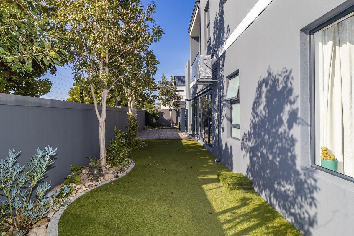 A well-maintained rear garden featuring artificial turf, a paved border, and a wooden deck area adjacent to the modern grey exterior wall.