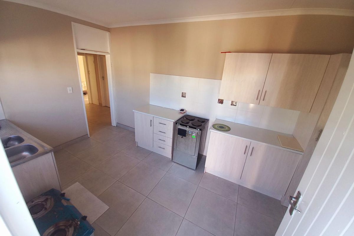 A functional kitchen featuring light-toned cabinetry, tiled flooring, a built-in stove, and a double-basin sink with tiled splashbacks.