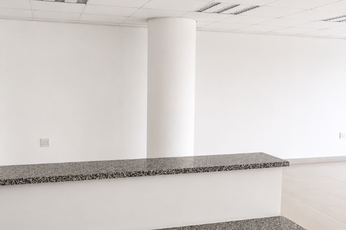 A bright, empty office space featuring a built-in reception desk with granite countertops, a suspended ceiling, and neutral tiled flooring.