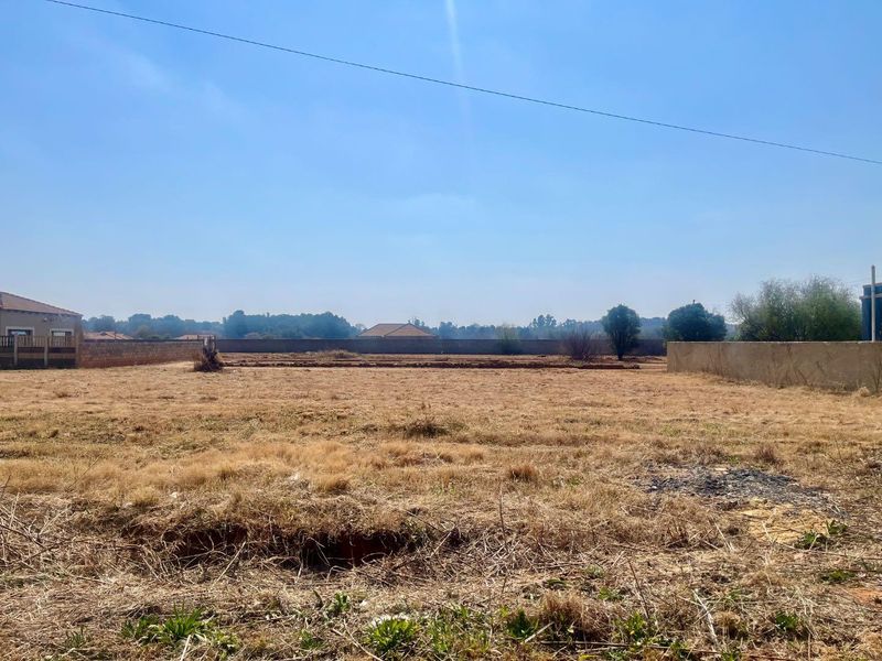 A vacant residential plot featuring dry grass, perimeter boundary walls, and clear views of the surrounding neighborhood.