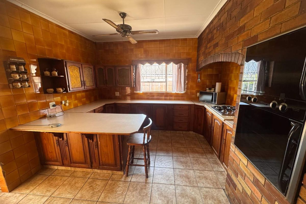A dated kitchen featuring extensive brown ceramic tiling, wooden cabinetry, a brick feature wall, and built-in cooking appliances.