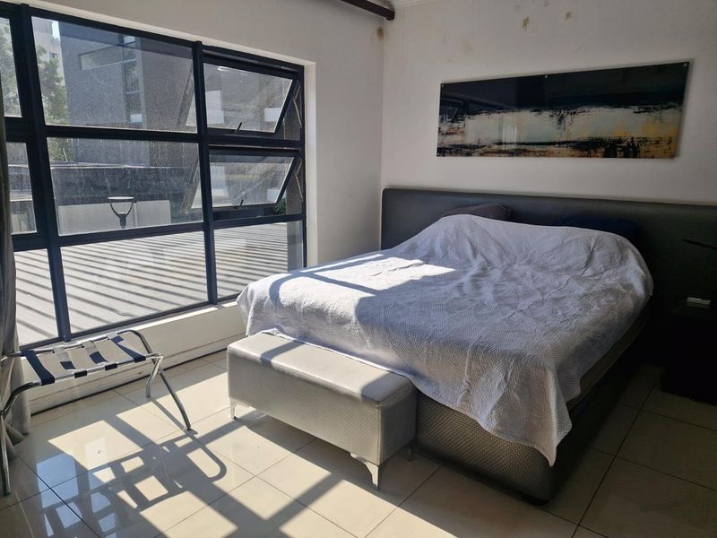 A bedroom featuring large aluminium-framed windows providing natural light and tiled flooring, showing visible signs of ceiling water damage.