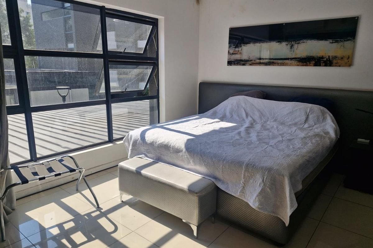 A bedroom featuring large aluminium-framed windows providing natural light and tiled flooring, showing visible signs of ceiling water damage.