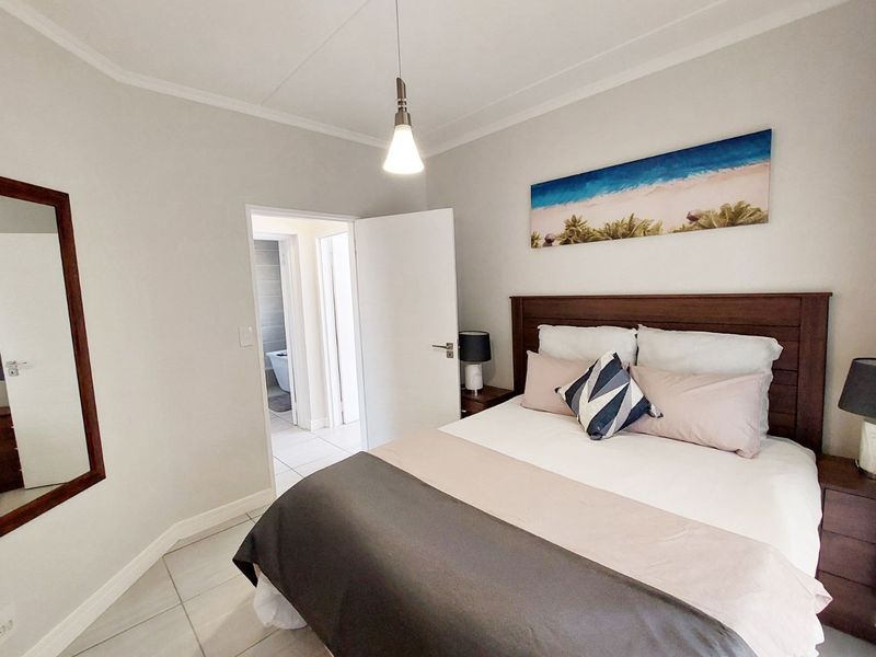 A well-maintained bedroom featuring neutral wall tones, tiled flooring, and a pendant light fixture, with direct access to an adjoining bathroom.