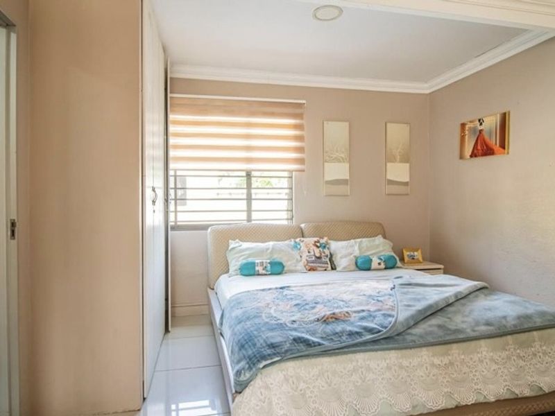 A functional bedroom featuring built-in cupboards, tiled flooring, and an adjoining en-suite bathroom, offering a practical layout with neutral wall finishes.