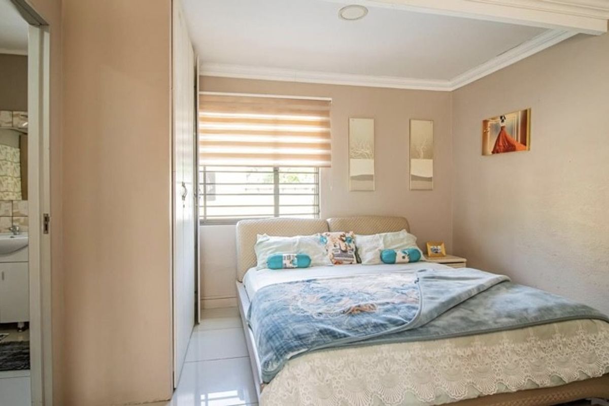 A functional bedroom featuring built-in cupboards, tiled flooring, and an adjoining en-suite bathroom, offering a practical layout with neutral wall finishes.