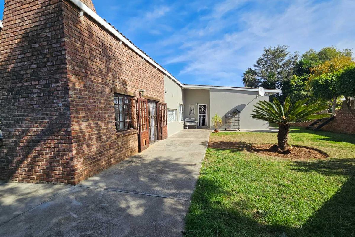 Rear view of the property featuring a brick facade, concrete patio area, and a well-maintained garden with established landscaping.