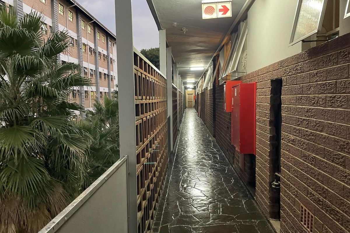 An exterior apartment building walkway featuring brick walls, stone-tiled flooring, and safety signage.