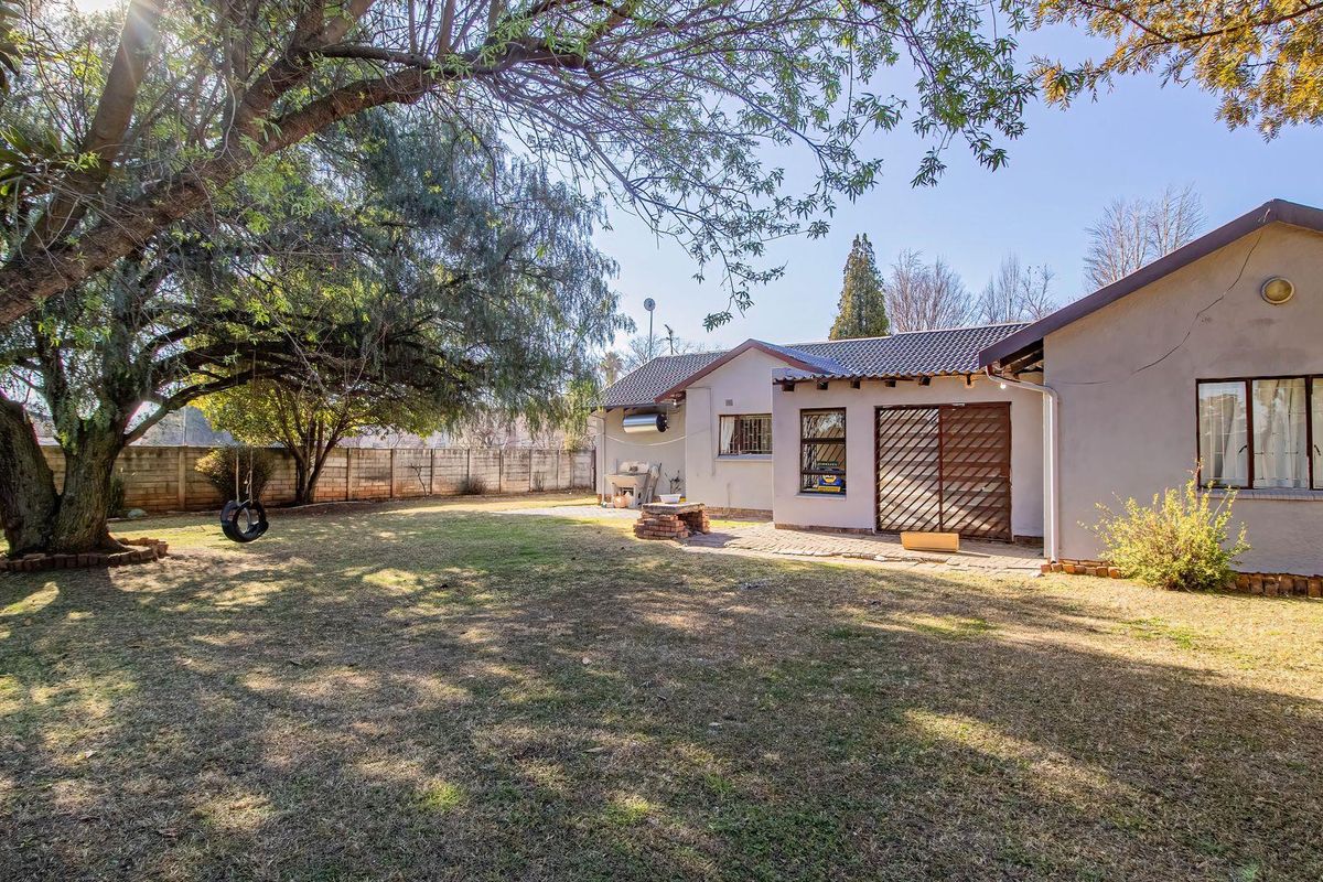 Spacious rear garden featuring a paved patio area, built-in braai, and established trees, enclosed by a secure brick boundary wall.