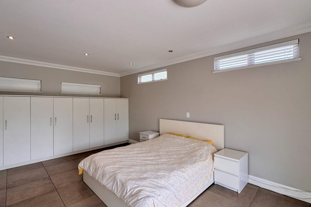 Spacious bedroom featuring neutral wall tones, tiled flooring, recessed downlighting, and extensive built-in cupboard storage with integrated horizontal window blinds.