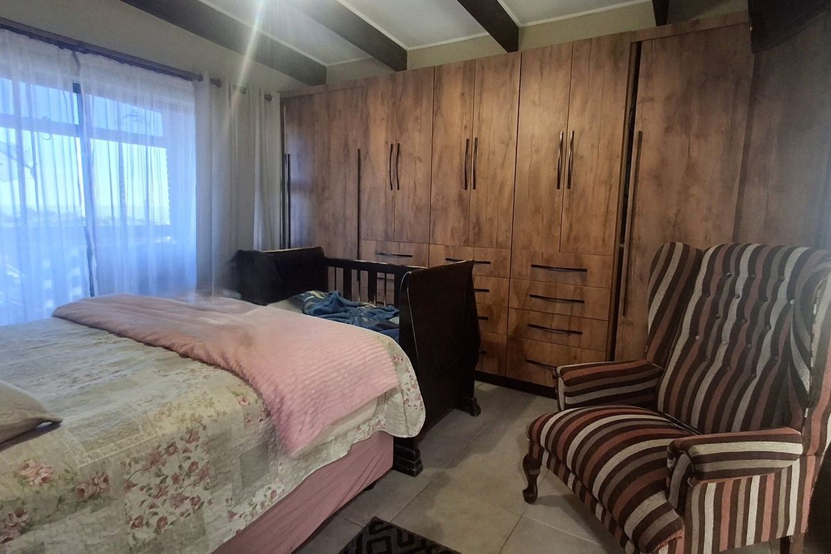 A bedroom featuring extensive built-in wooden cupboards, exposed ceiling beams, and tiled flooring, with direct access to an outdoor area via a sliding glass door.