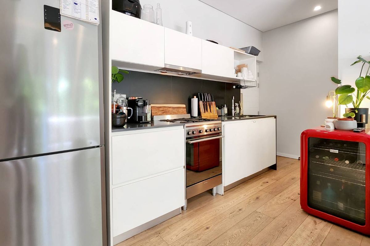 Modern kitchen featuring sleek white cabinetry, a stainless steel oven with gas cooktop, integrated extractor fan, and durable timber-look flooring.