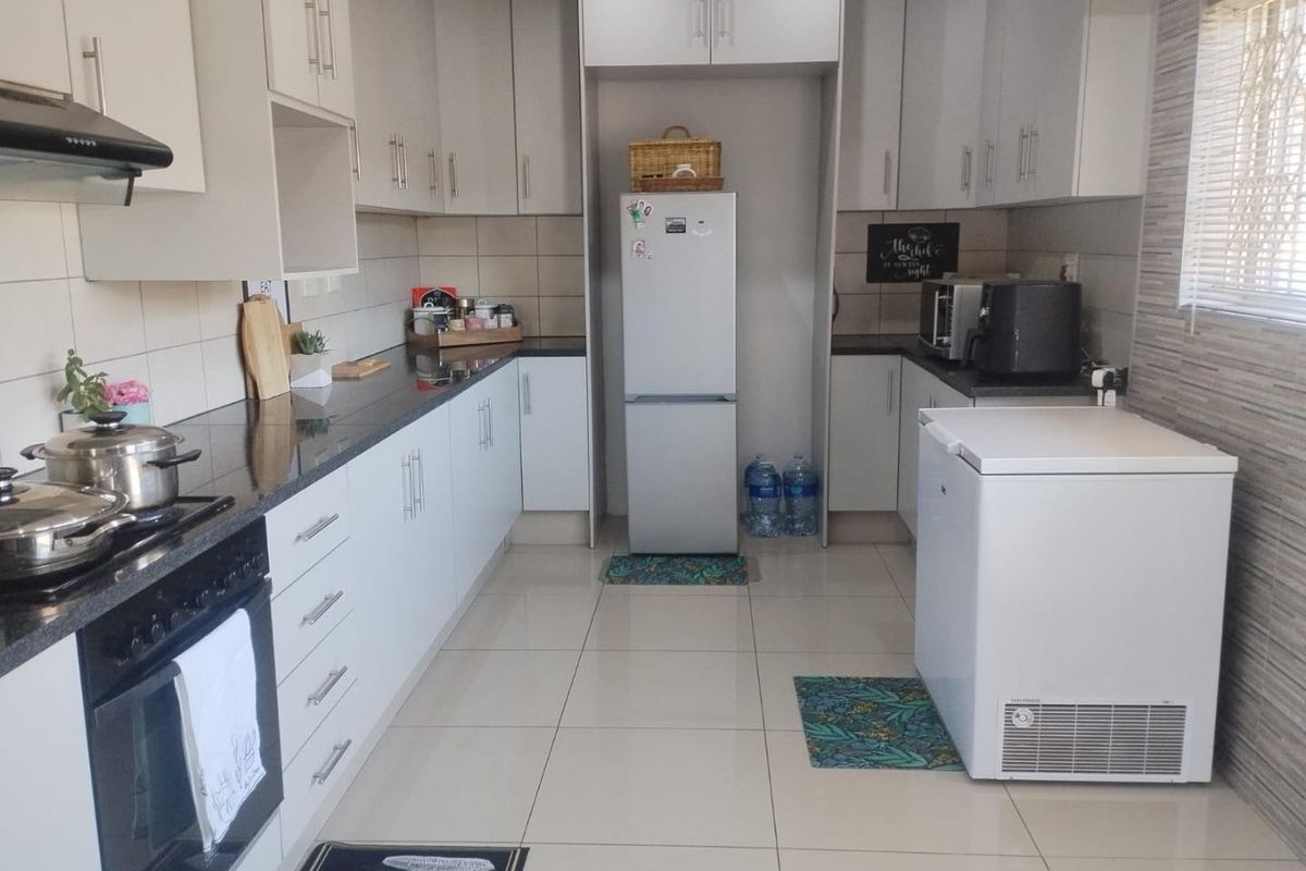 A functional kitchen featuring white cabinetry, dark granite countertops, tiled flooring, and a built-in oven with an extractor fan.