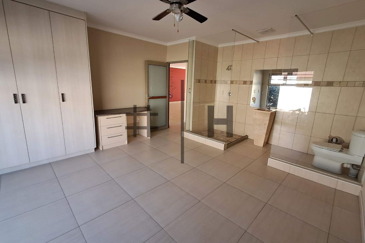 Spacious bedroom featuring built-in cupboards, an open-plan en-suite bathroom with a glass-enclosed shower, and tiled flooring throughout.