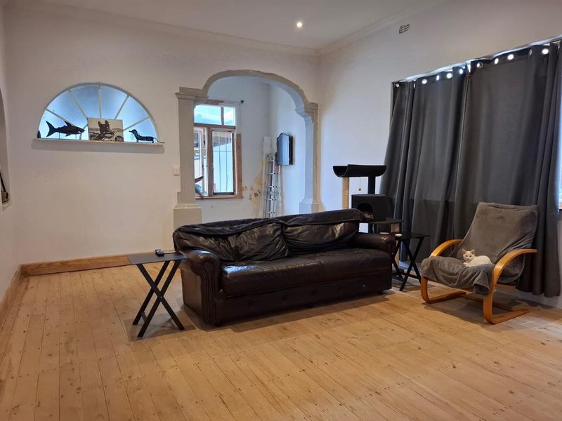 Spacious living room featuring original hardwood flooring, a decorative archway, and an arched window, offering a character-filled space with potential for cosmetic updates.