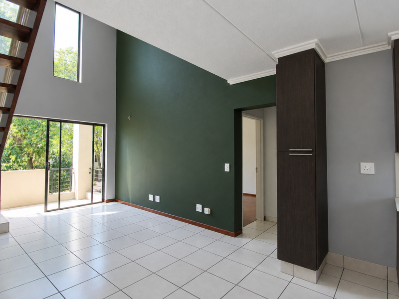 Spacious open-plan living area featuring high ceilings, tiled floors, a modern wooden staircase, and direct access to a private balcony.