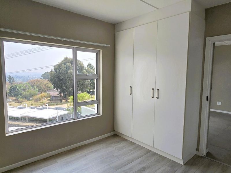 A bright, empty bedroom featuring modern laminate flooring, a large window with a view, and built-in white wardrobes.