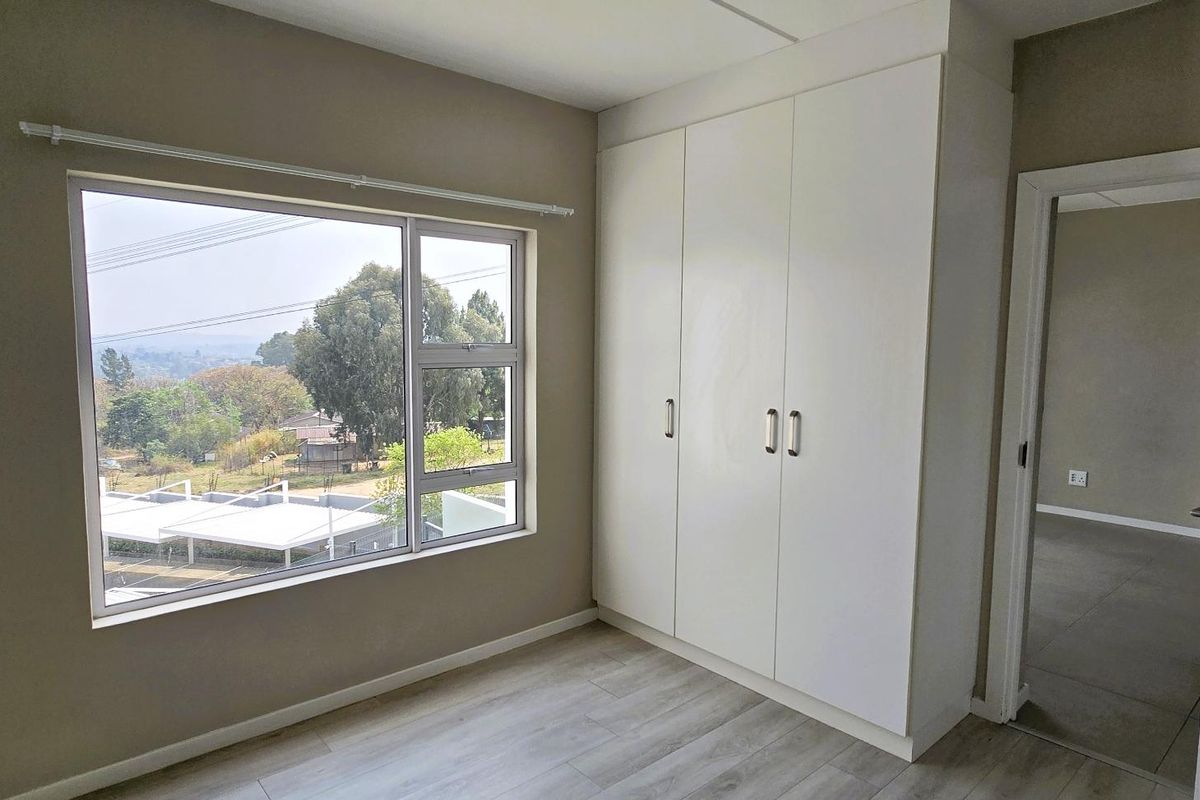 A bright, empty bedroom featuring modern laminate flooring, a large window with a view, and built-in white wardrobes.