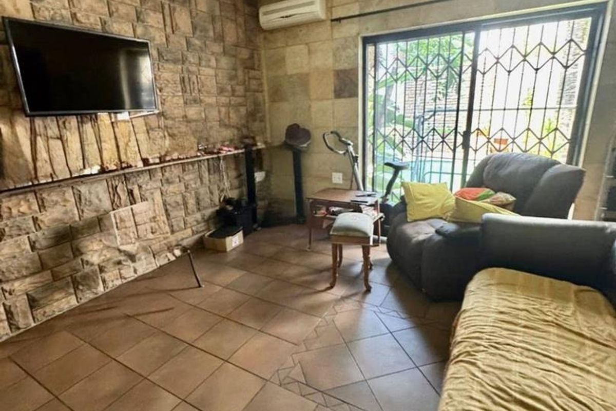 Living room featuring natural stone wall cladding, tiled flooring, a wall-mounted air conditioning unit, and sliding glass doors with security gates.