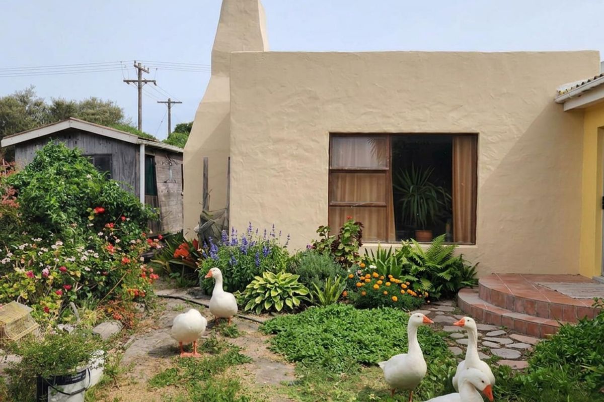 A view of the rear exterior of the farm property, featuring a textured facade, a prominent chimney, and a landscaped garden area.