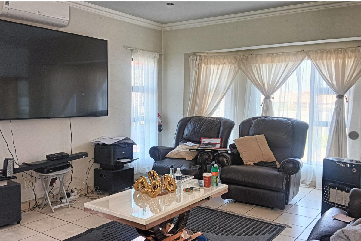 A living room featuring tiled flooring, large windows with curtains, and a wall-mounted air conditioning unit.