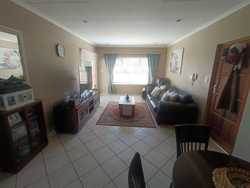 A comfortable living room featuring tiled flooring, recessed downlighting, and natural light through a large window with blinds.