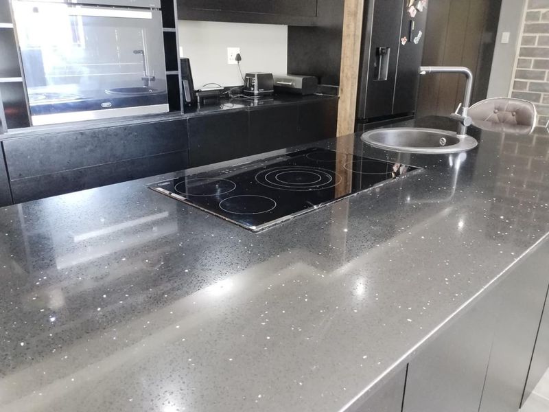 Modern kitchen featuring a large black stone island with an integrated electric hob, undermount sink, and sleek black cabinetry.