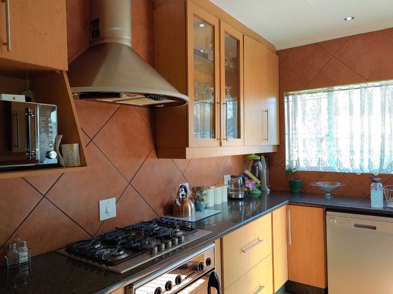 A functional kitchen featuring wooden cabinetry, granite countertops, a gas cooktop with a stainless steel extractor fan, and decorative tiled backsplash.