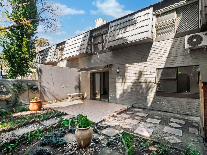 Rear view of the apartment featuring a private tiled patio, garden area, and brick facade with an installed air conditioning unit.