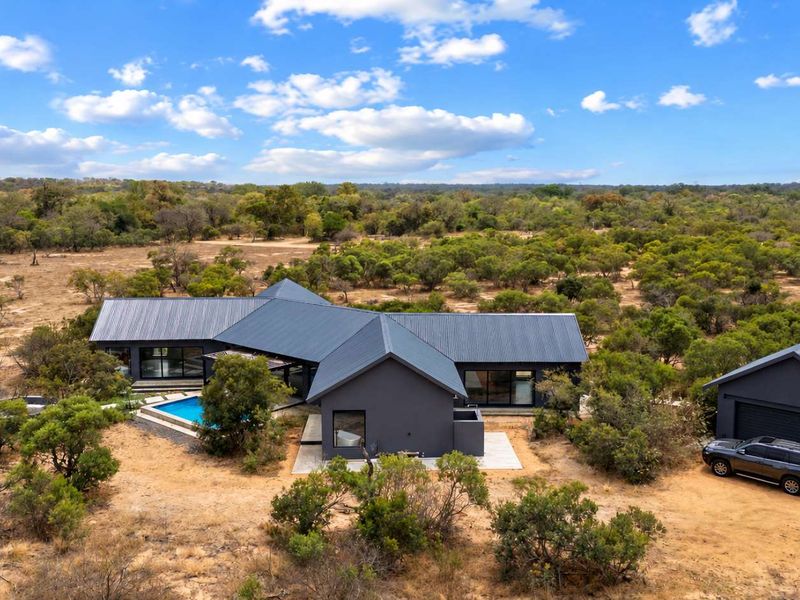 Aerial view of a modern dark-toned residence featuring a metal roof, swimming pool, and detached garage set within a natural bushveld landscape.