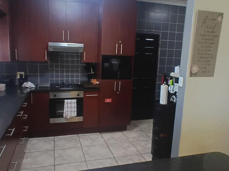A functional kitchen featuring dark wood cabinetry, granite countertops, a gas hob, and an integrated oven with a tiled backsplash.