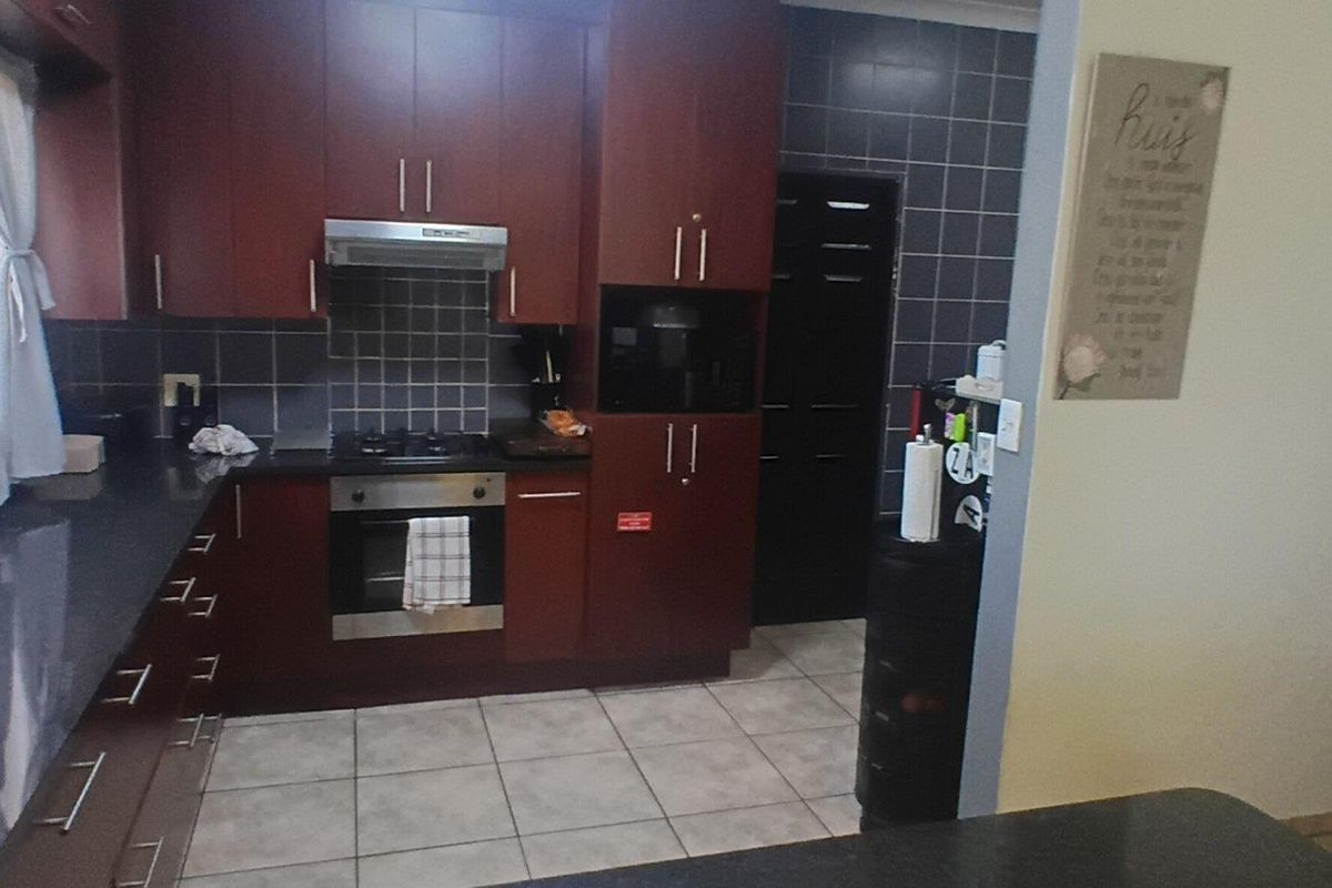 A functional kitchen featuring dark wood cabinetry, granite countertops, a gas hob, and an integrated oven with a tiled backsplash.
