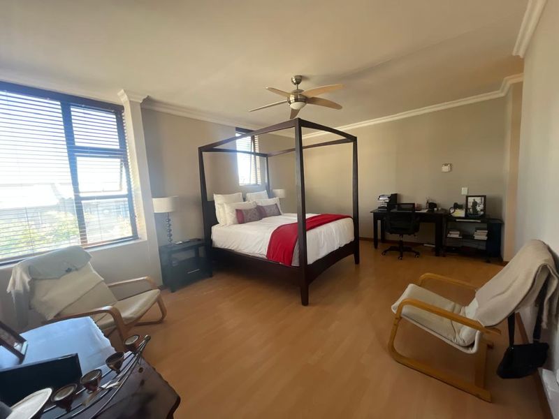 Spacious bedroom featuring laminate flooring, a ceiling fan, and large windows with venetian blinds, offering a comfortable and well-lit living space.