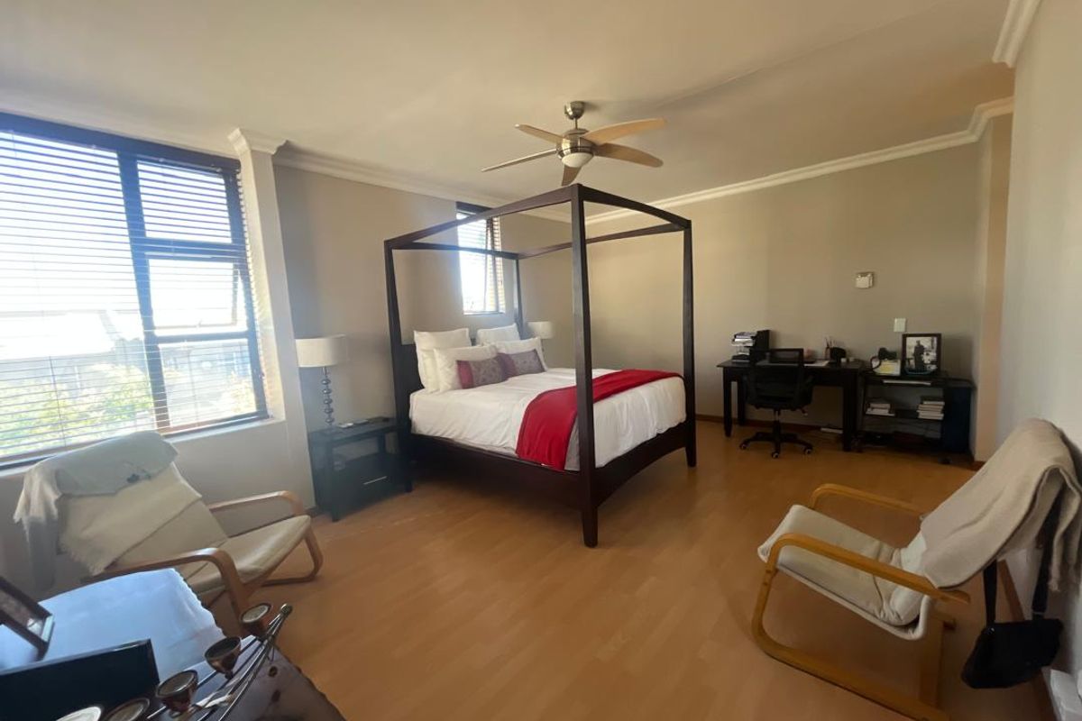 Spacious bedroom featuring laminate flooring, a ceiling fan, and large windows with venetian blinds, offering a comfortable and well-lit living space.
