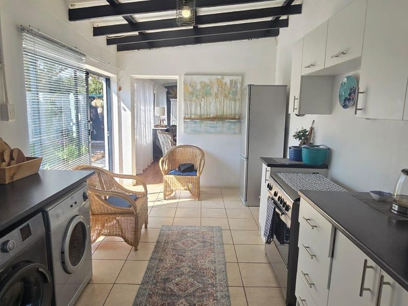 A functional kitchen featuring exposed timber ceiling beams, tiled flooring, white cabinetry, and direct access to the outdoor area via a sliding glass door.
