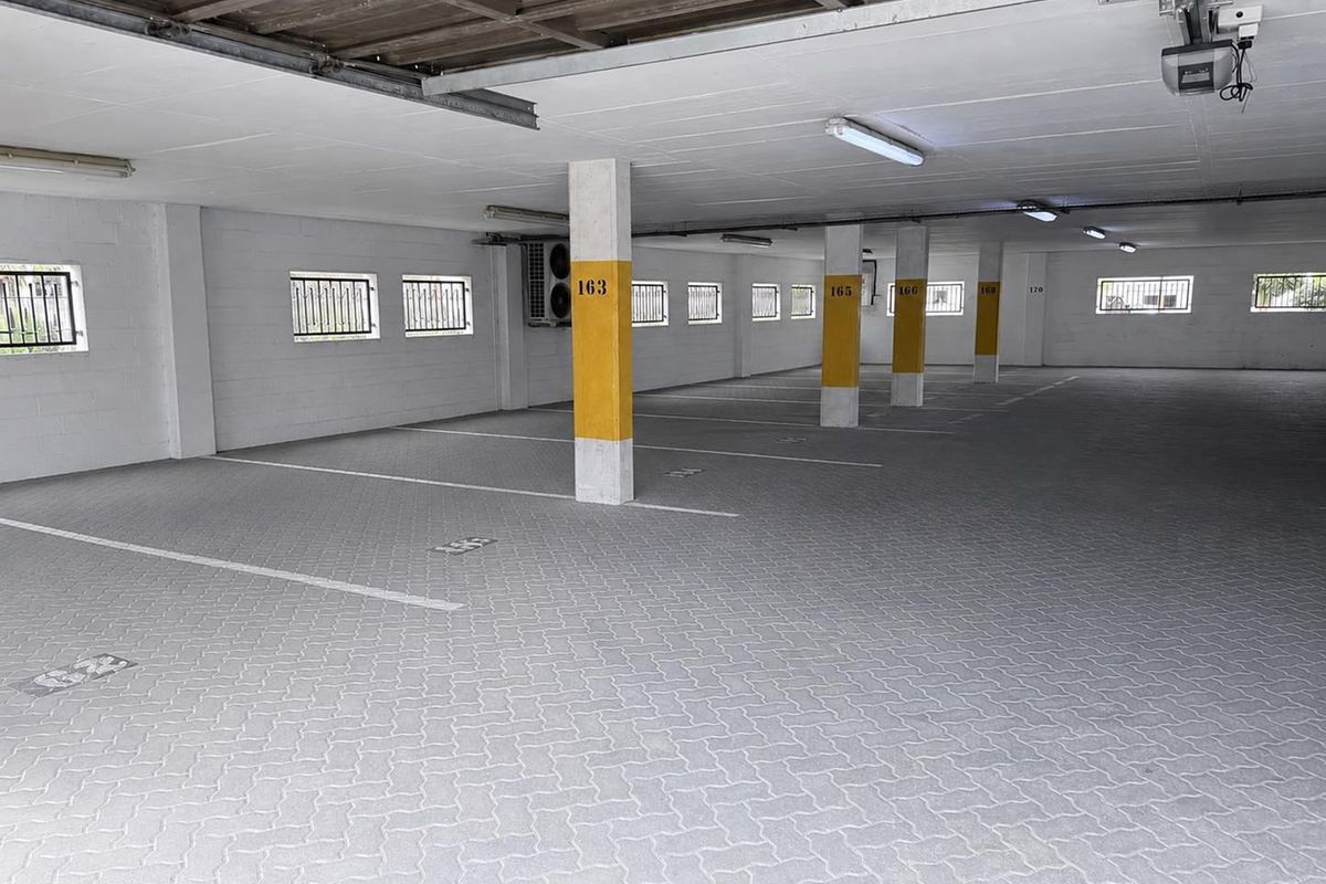 A clean, well-maintained covered parking garage featuring paved flooring, structural support columns, and secure window grilles.