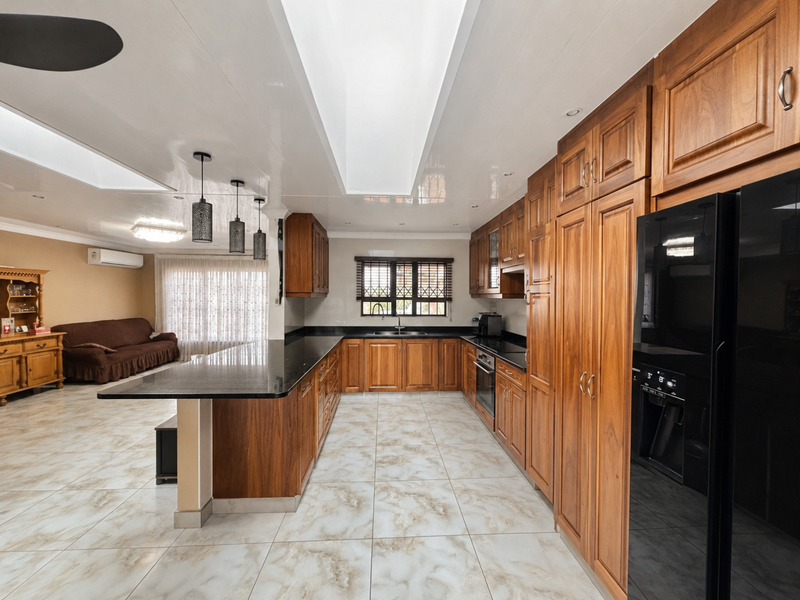 Spacious open-plan kitchen featuring warm wooden cabinetry, granite countertops, integrated appliances, and abundant natural light from overhead skylights.