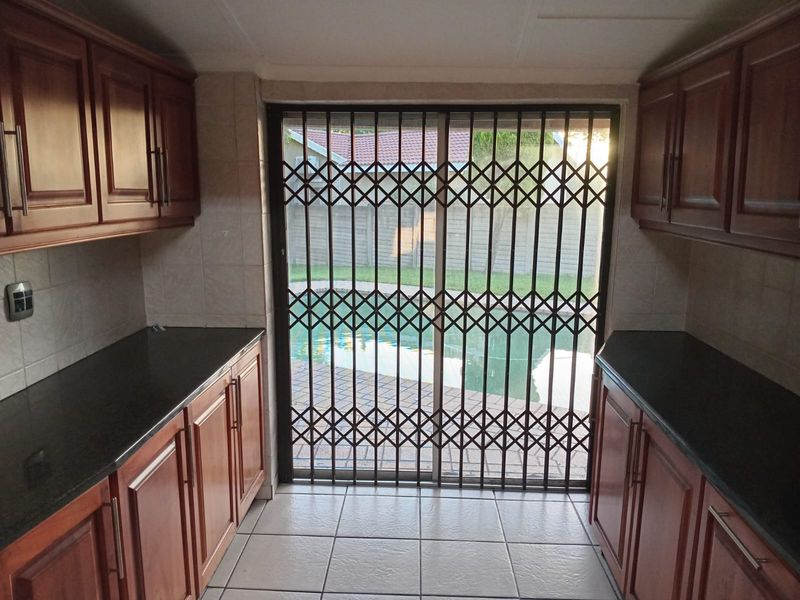 A functional scullery or utility area featuring built-in wooden cabinetry, granite countertops, and direct access to the pool area through a sliding glass door.
