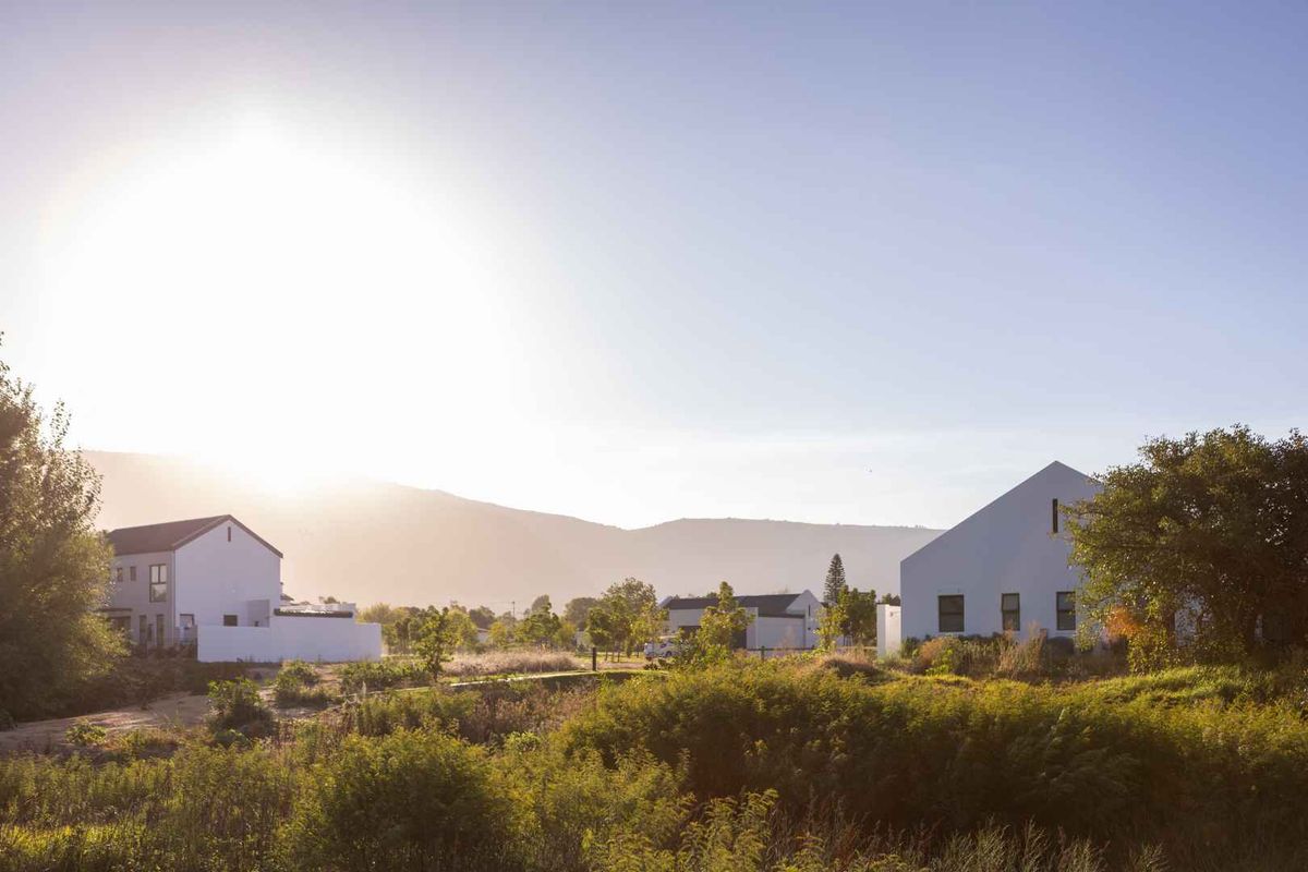 A scenic view of modern white residential homes set within a landscaped estate with mountain views in the background.