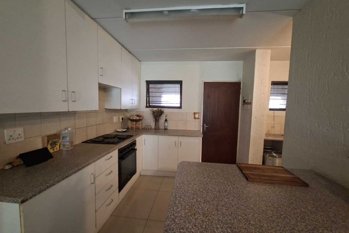 A functional kitchen featuring white cabinetry, stone-look countertops, a built-in oven and hob, and tiled flooring with an adjacent scullery area.
